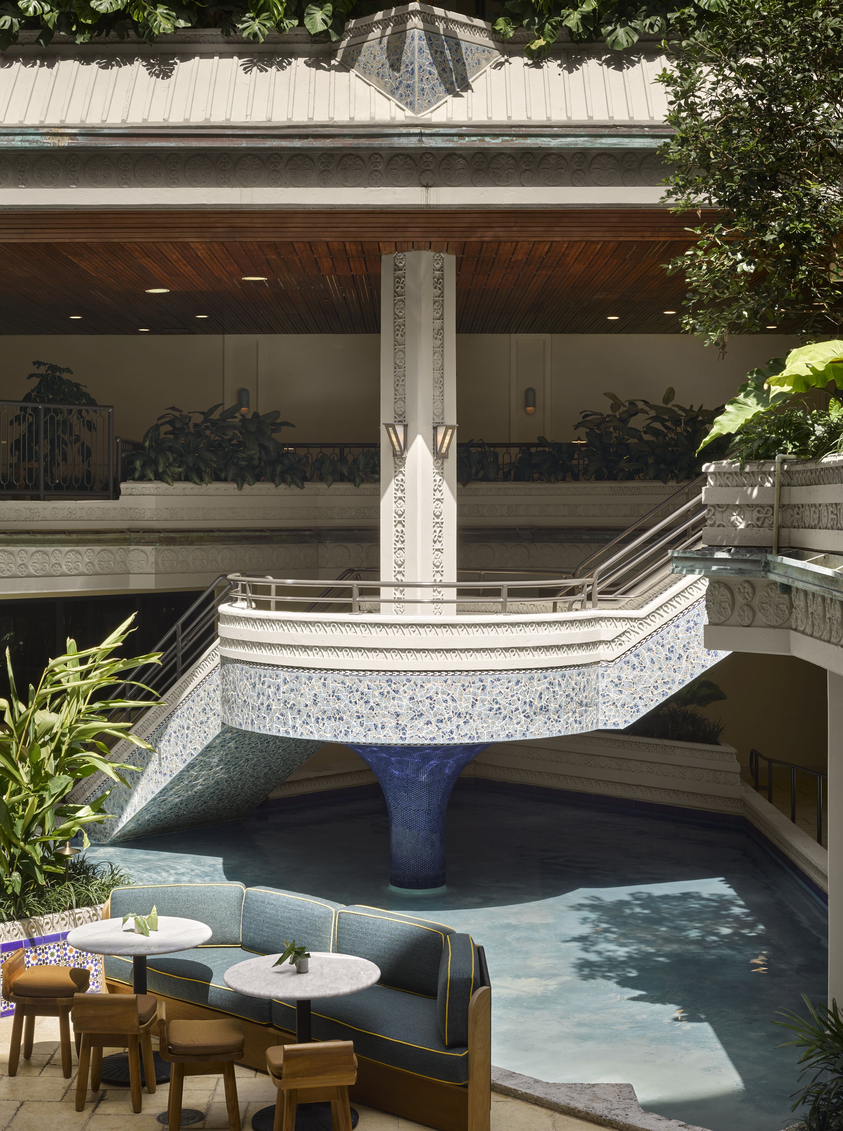 Ein Poolbereich mit einer blauen Mosaikfontäne, Sitzgelegenheiten und einer Treppe.