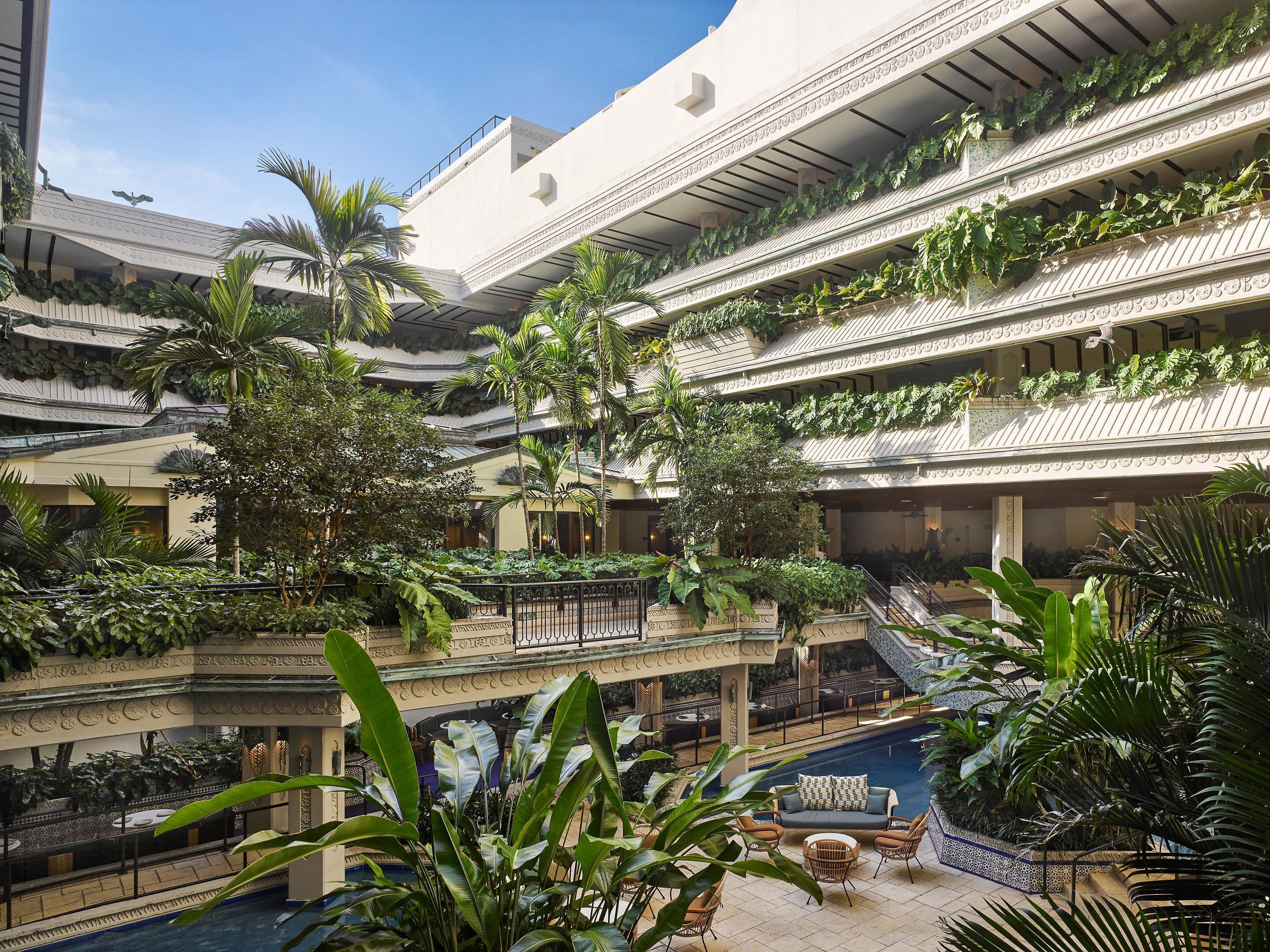 Un vestíbulo de hotel de varios niveles con balcones, plantas de interior y una zona de piscina.