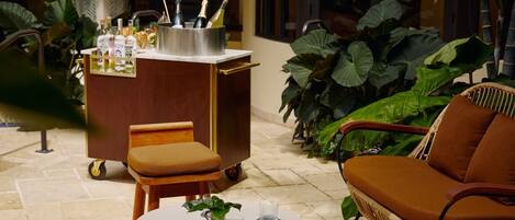 A cozy outdoor seating area with wicker furniture and a small table, surrounded by large green plants.