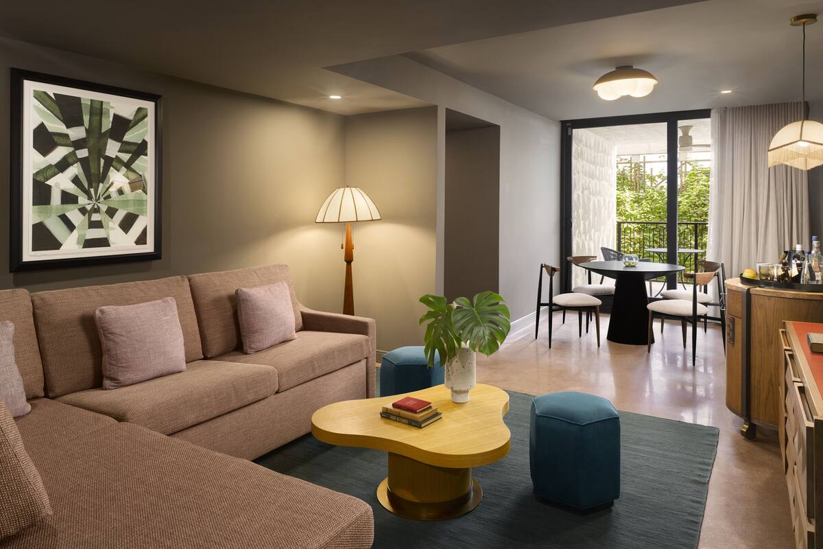 A modern living room with a sofa, coffee table, and a dining area with chairs and a table.