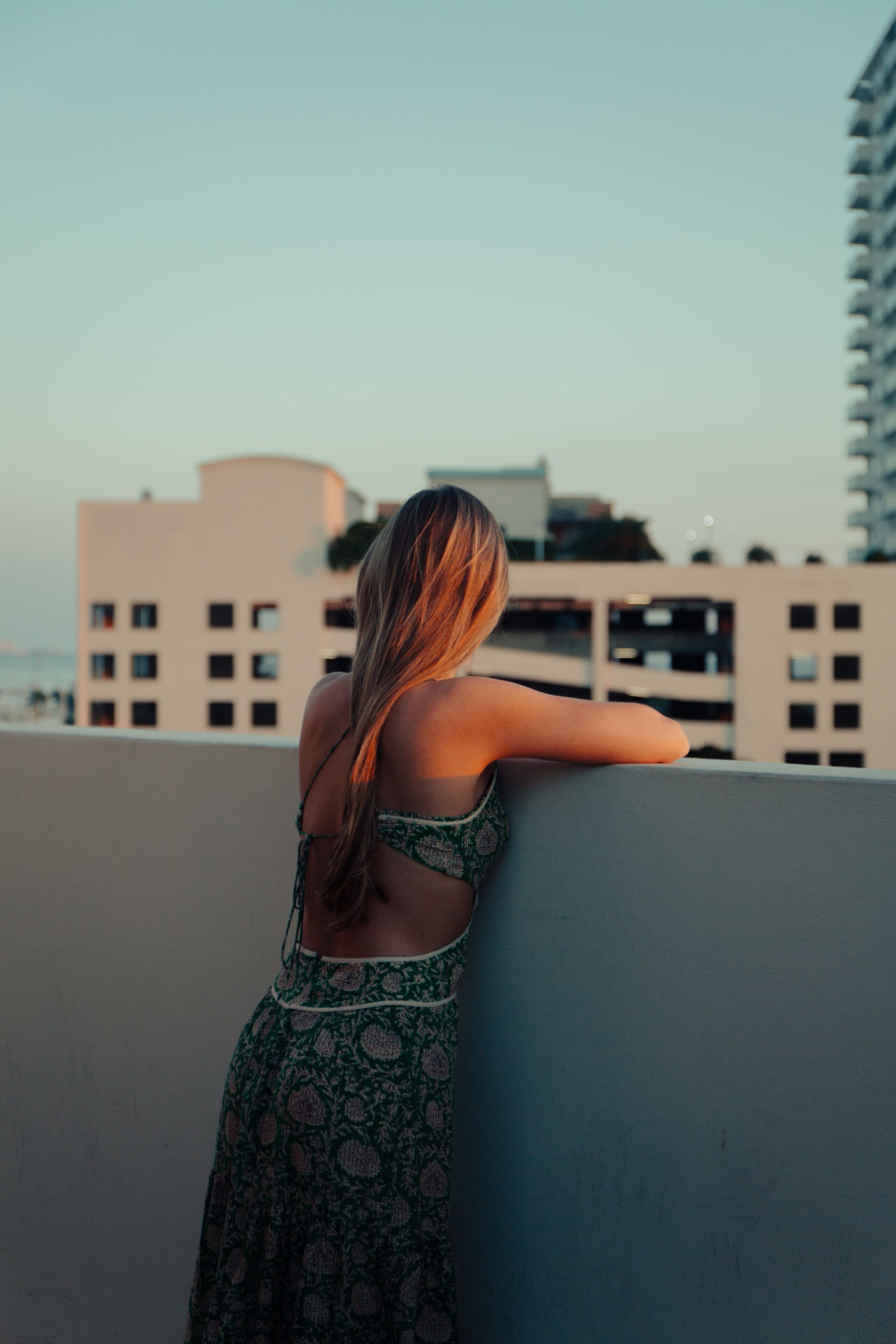 A woman leaning on a balcony railing with a cityscape in the background.