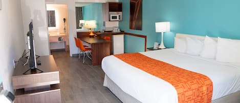 A hotel room with a bed, desk, chair, and a small kitchenette.