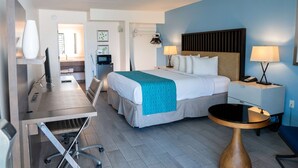 A hotel room with a bed, bedside tables, a desk with a chair, a small round table, and a view of the bathroom.