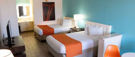 A hotel room with two beds, a desk, a chair, a lamp, and a small table.