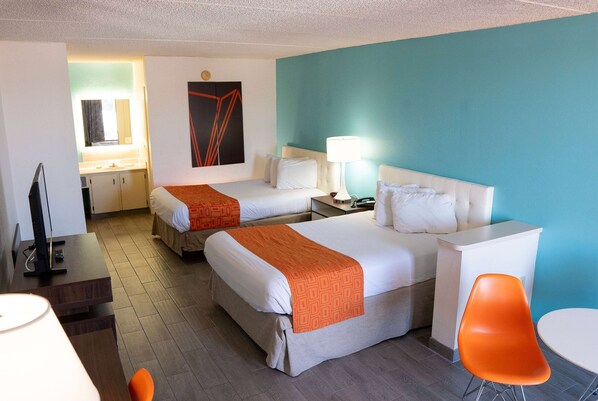 Habitación de hotel con dos camas, un escritorio, una silla, una lámpara y una mesita.