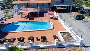 A hotel with a swimming pool, outdoor seating, and a parking area.