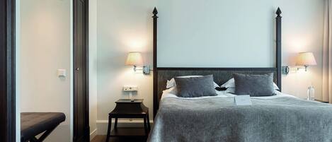 A neatly arranged hotel room with a large bed, bedside lamps, a small table, and a bench.