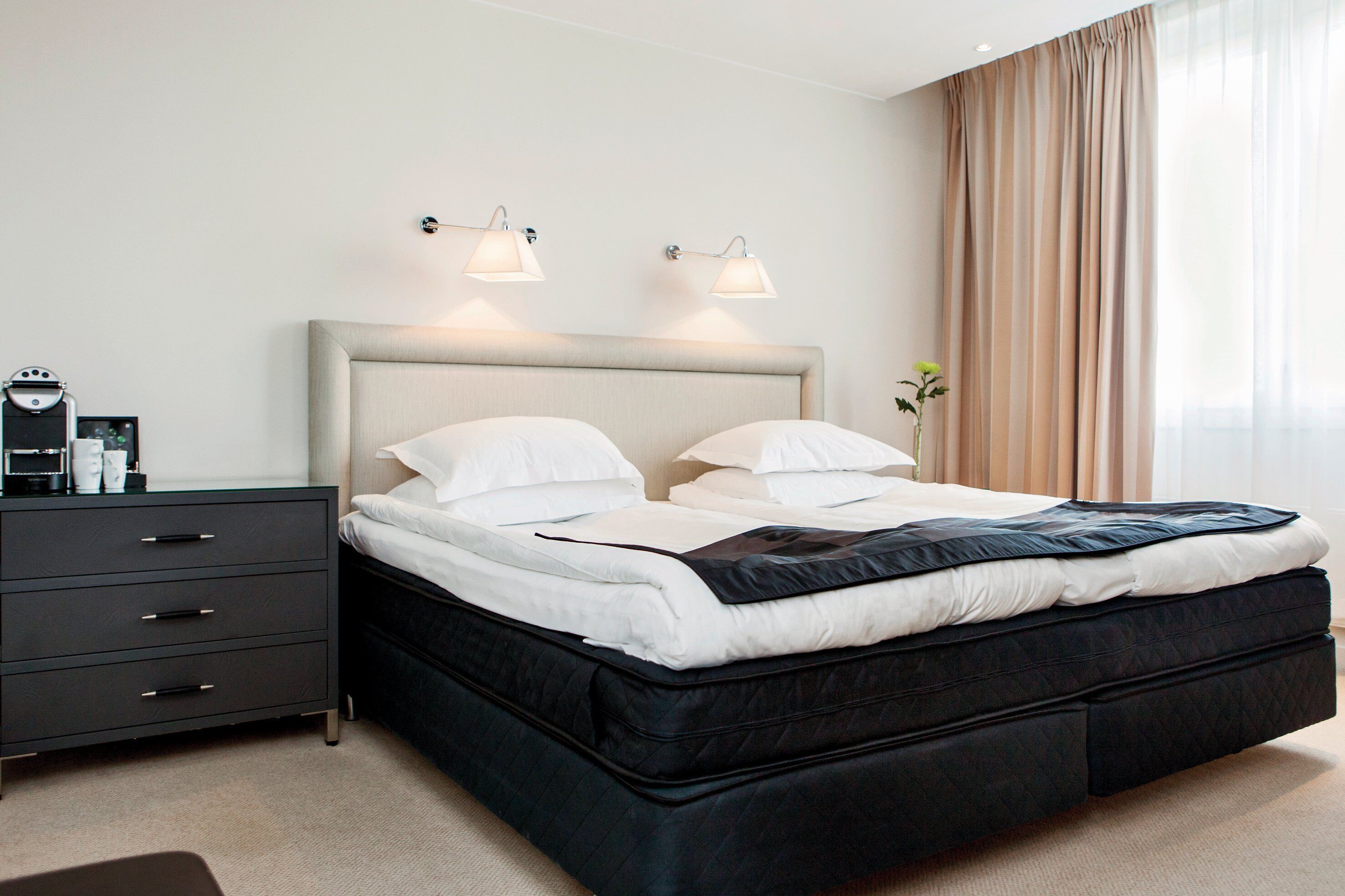 Una habitaci ón de hotel moderna con una cama grande, una mesita de noche y otra mesita auxiliar.