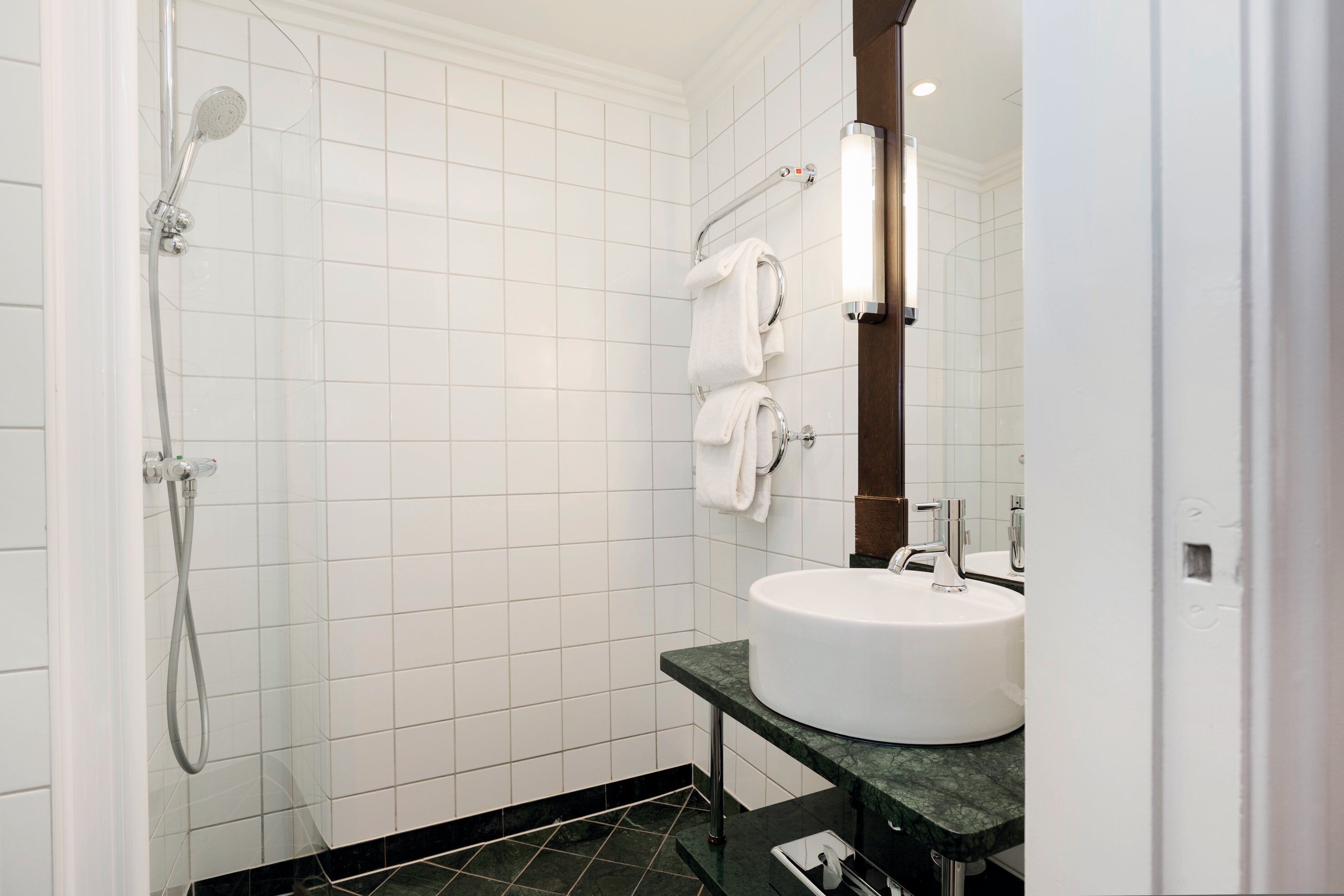 A modern bathroom with white tiles, a shower, a sink, and a towel rack.