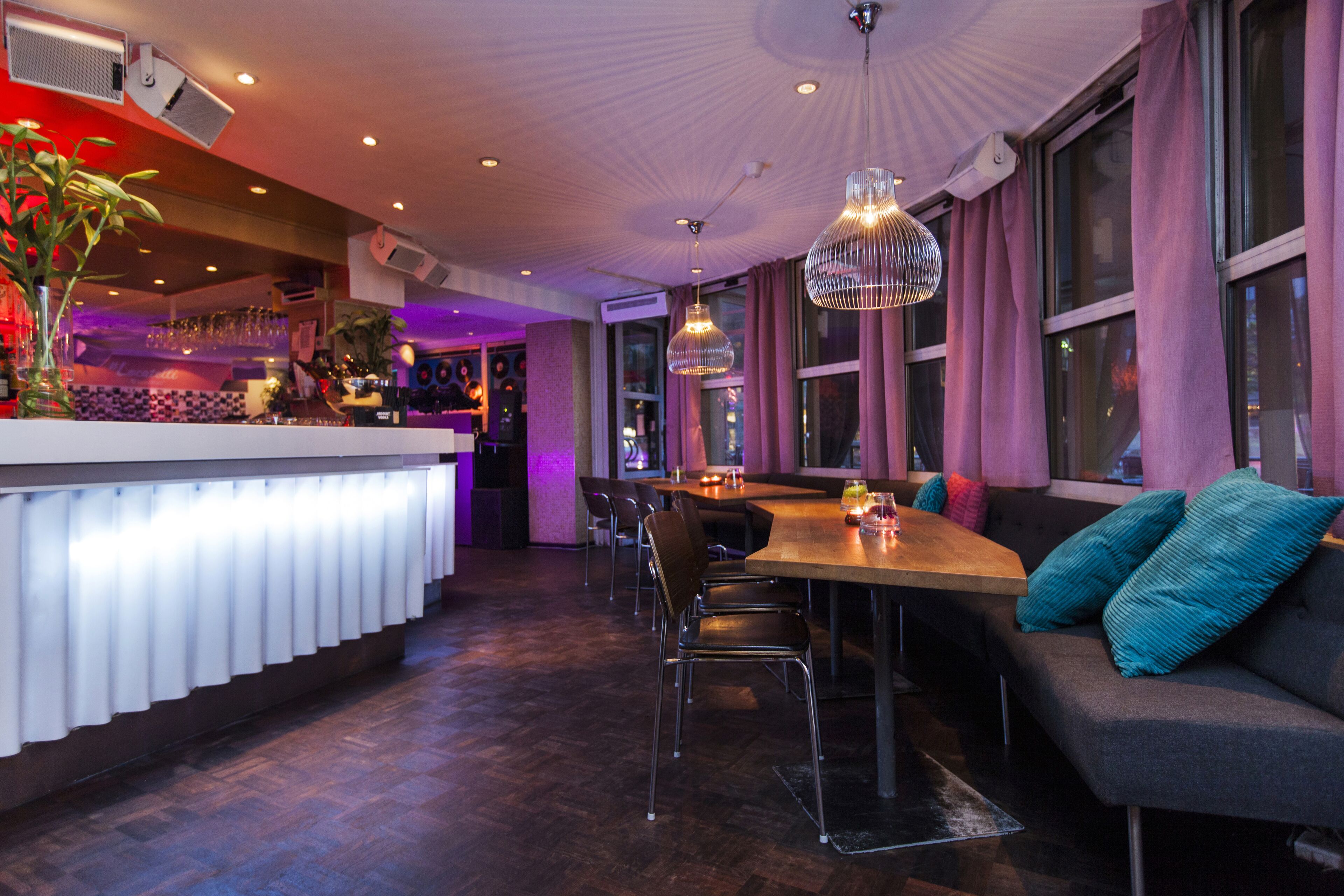 A modern restaurant with a bar area, seating, and a large window with curtains.