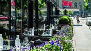 Un área de comedor al aire libre con mesas dispuestas para los huéspedes, rodeada por una fila de flores moradas.