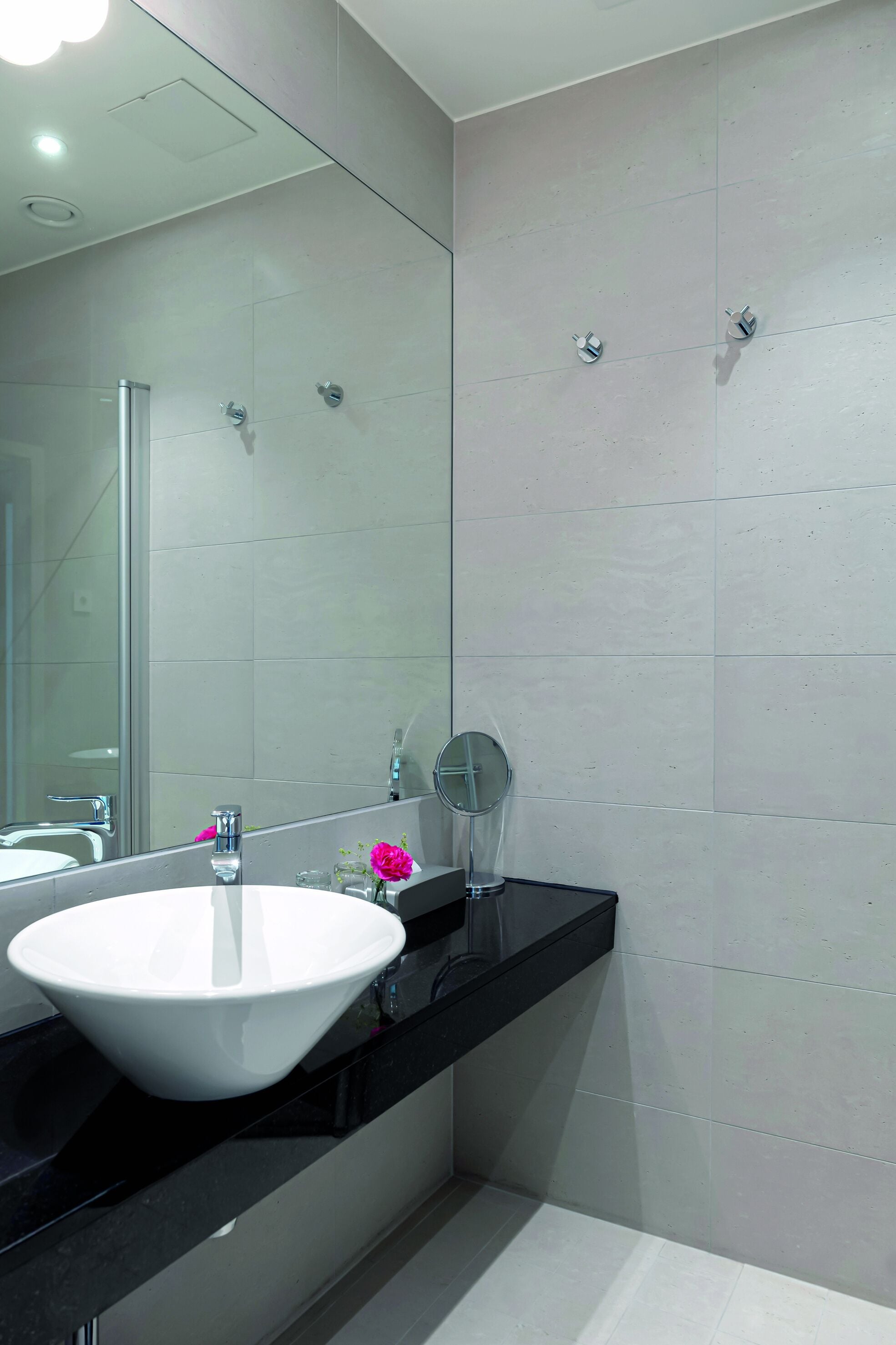 A modern bathroom with a large mirror, a white sink, and a black countertop.