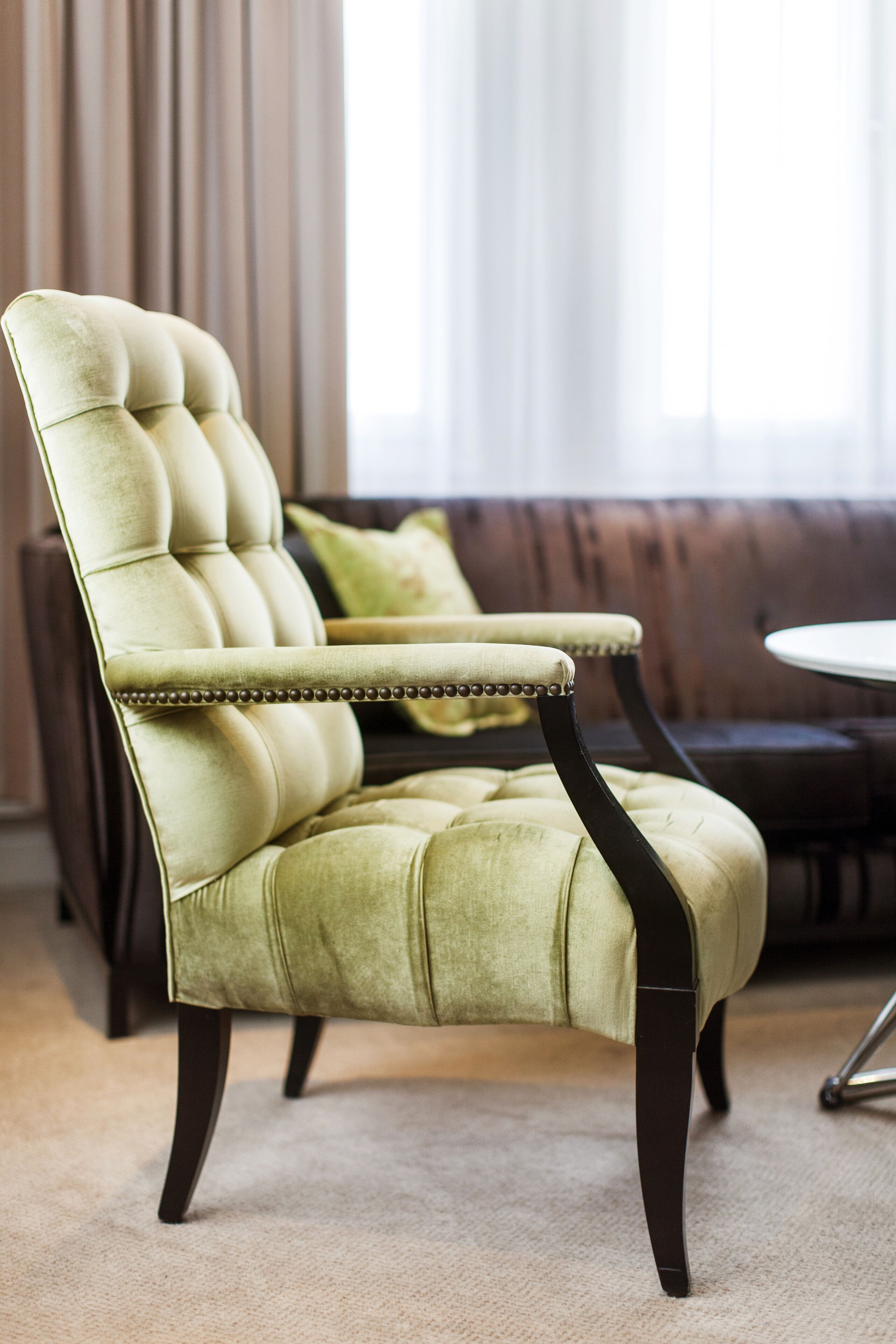 A tufted armchair with a high back and armrests, dark wooden legs, and a beige carpeted floor.