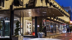 Un hotel con fachada de vidrio moderna, acceso cubierto y estacionamiento visible.