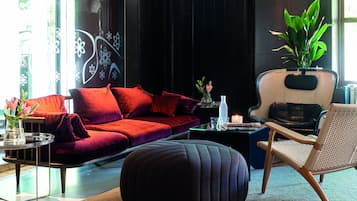 A modern living room with a red sofa, a round ottoman, a wicker chair, and a potted plant.