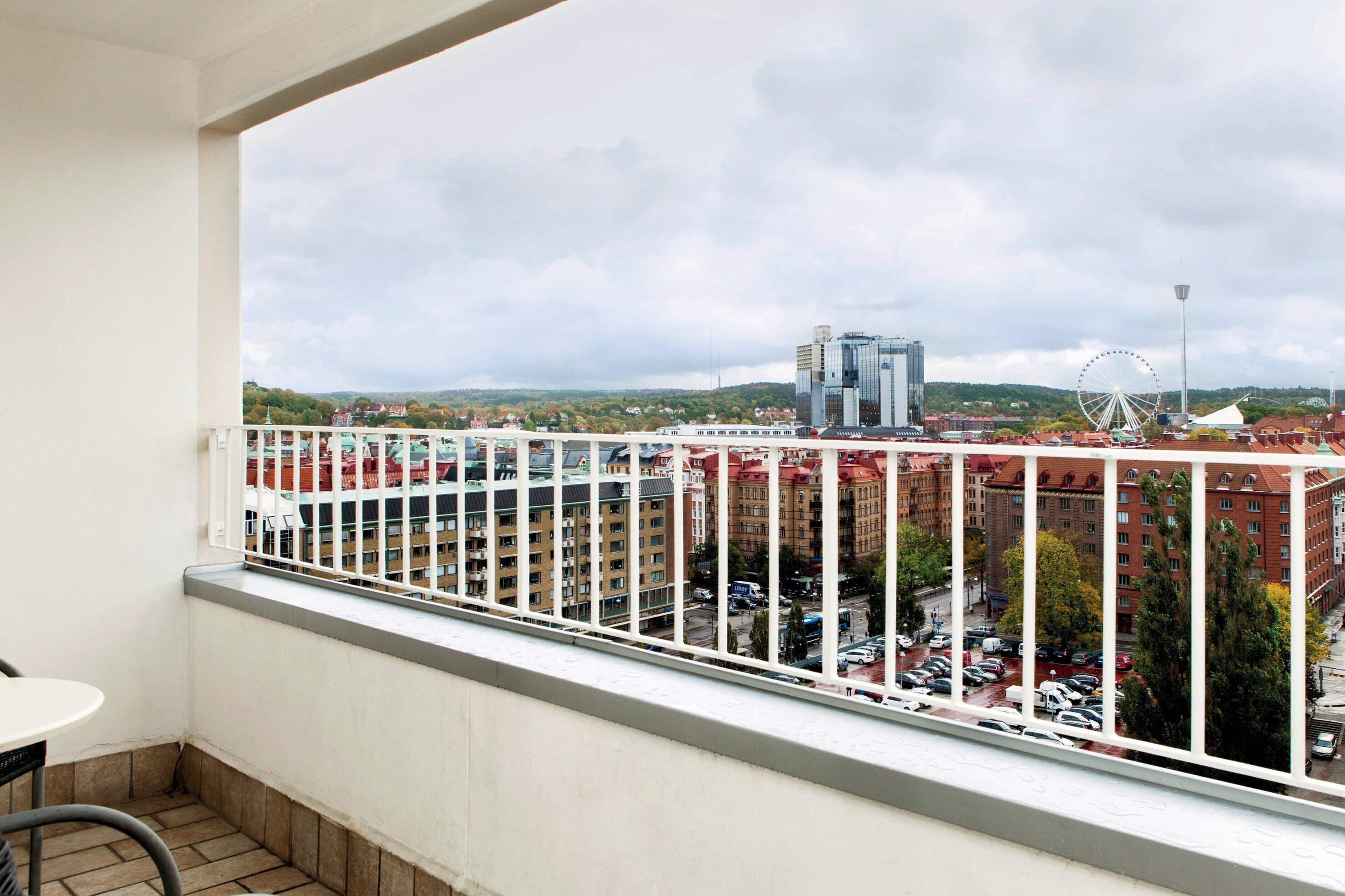 A balcony with a view of a cityscape, including buildings and a Ferris wheel.