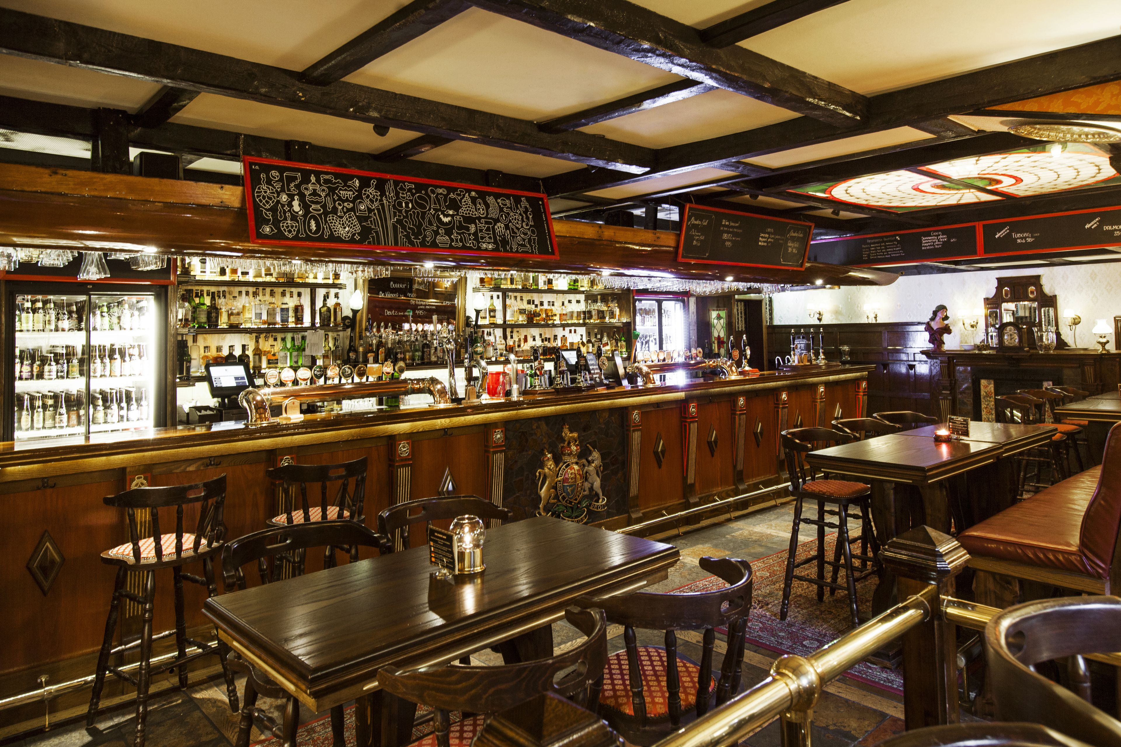 Una zona de bar con mobiliario de madera, una barra con varias botellas y un emblema decorativo en la pared.