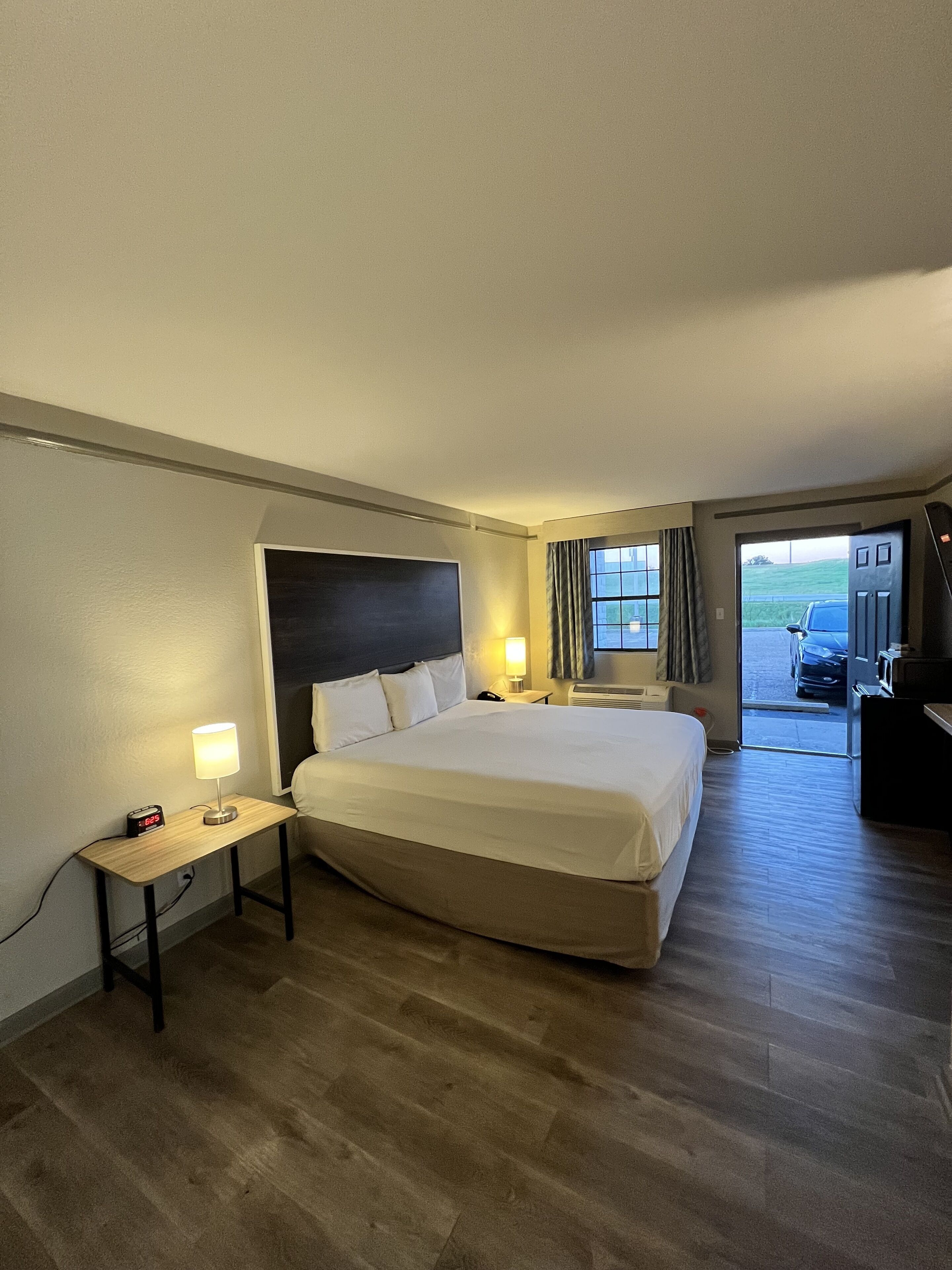 Et hotelværelse med en stor seng, sengeborde, et skrivebord og et vindue med gardiner.