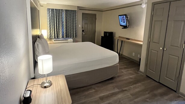 A hotel room with a bed, a desk with a lamp, a television, and a wardrobe. - Sulphur Extended Stay (Sulphur)