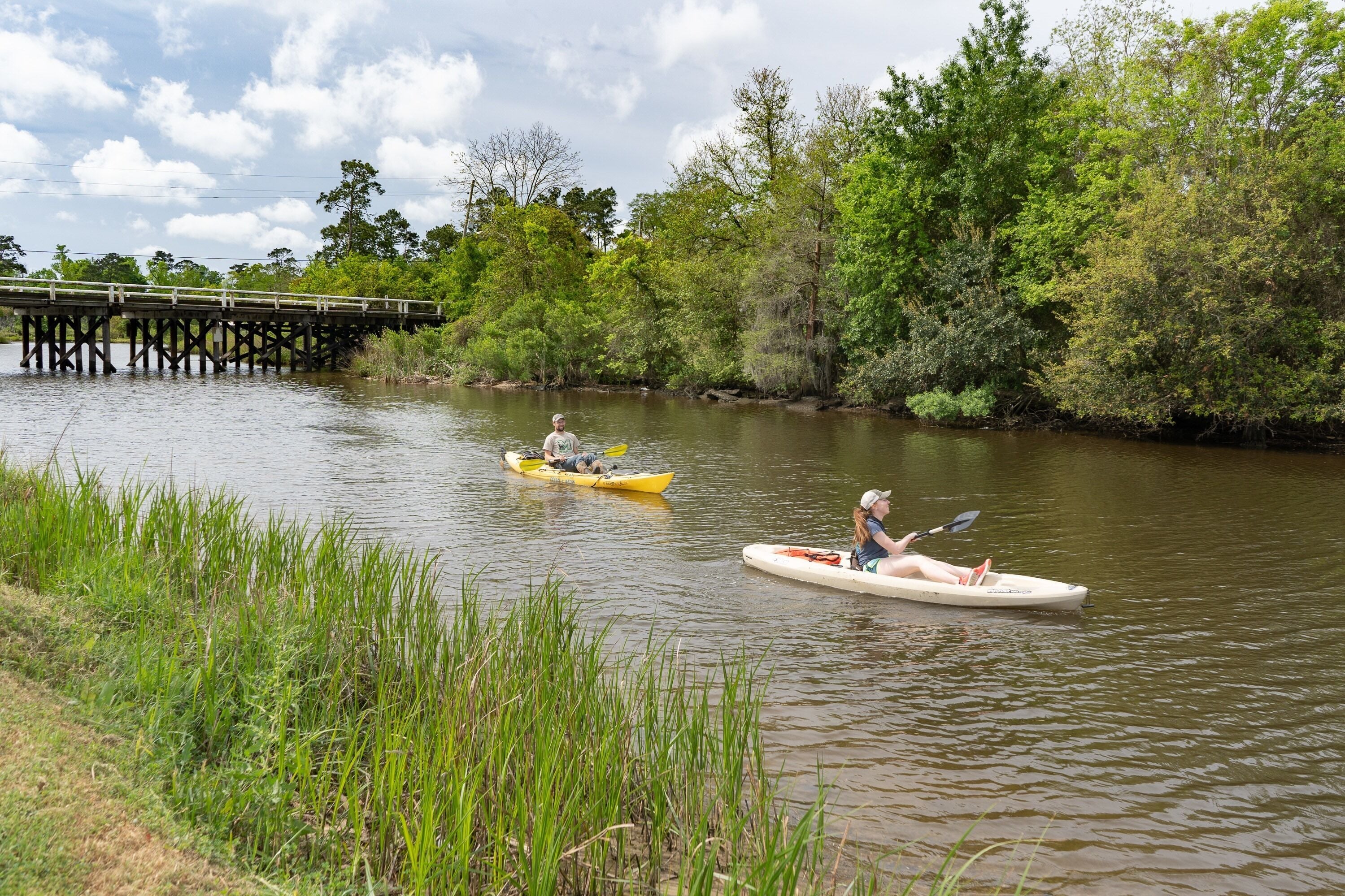 A calm river with two kayaks, a wooden bridge, and lush greenery.