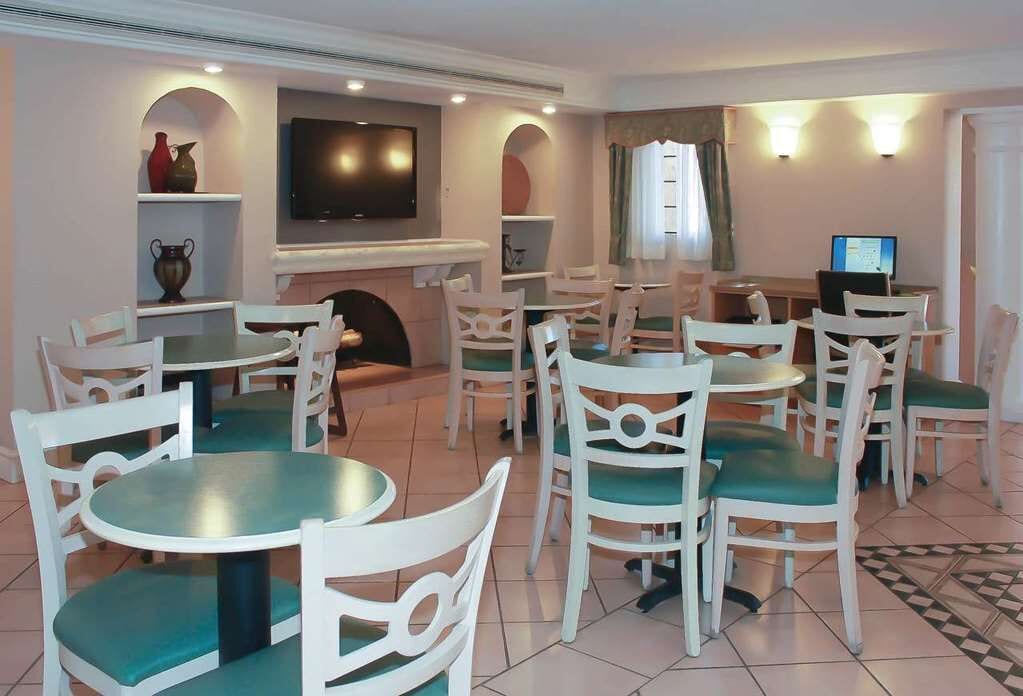 A dining area with white chairs and green cushions, a flat-screen TV mounted above a fireplace, and a computer on a desk.