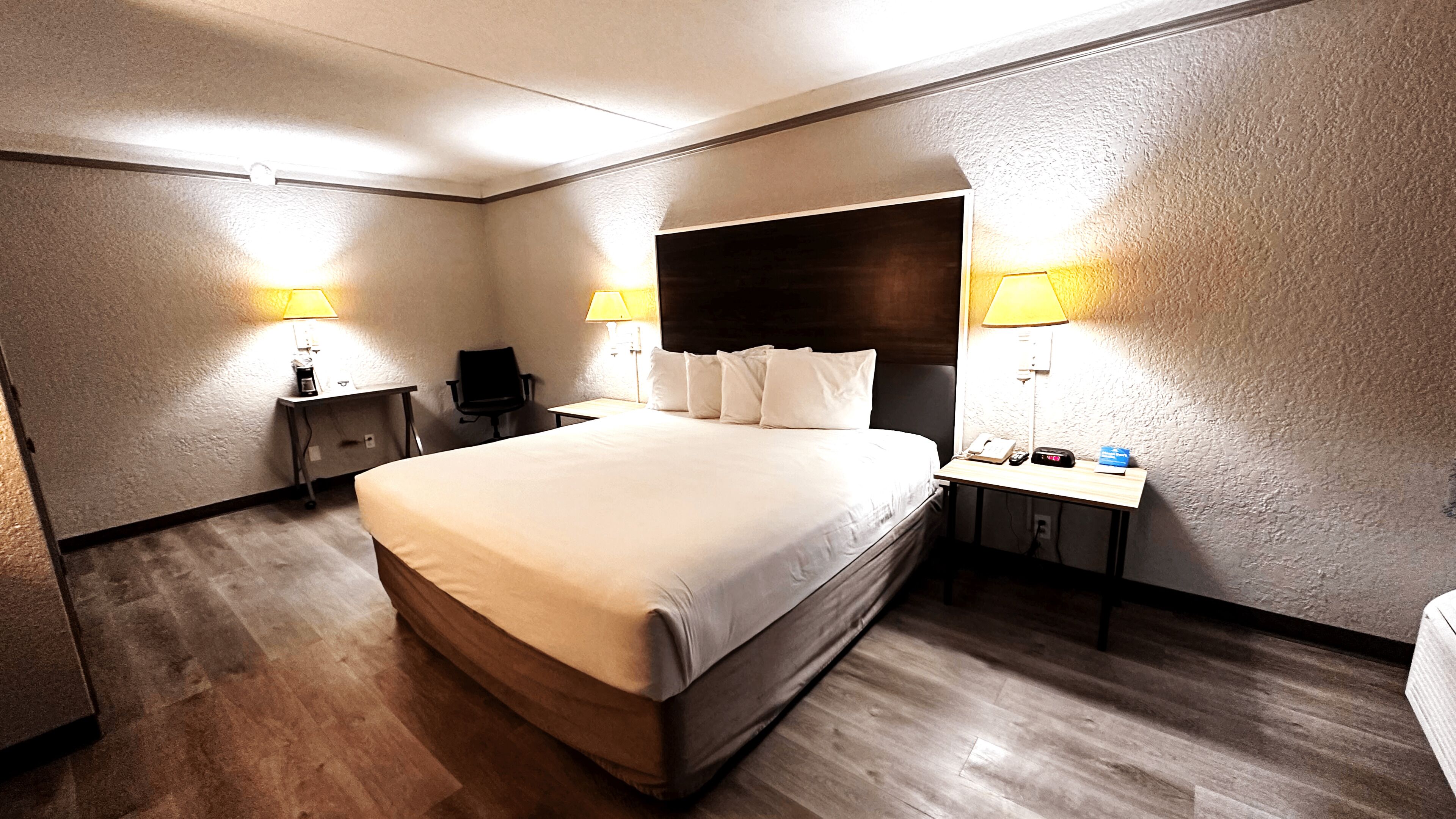 A hotel room with a large bed, two bedside tables, a desk, and two lamps.