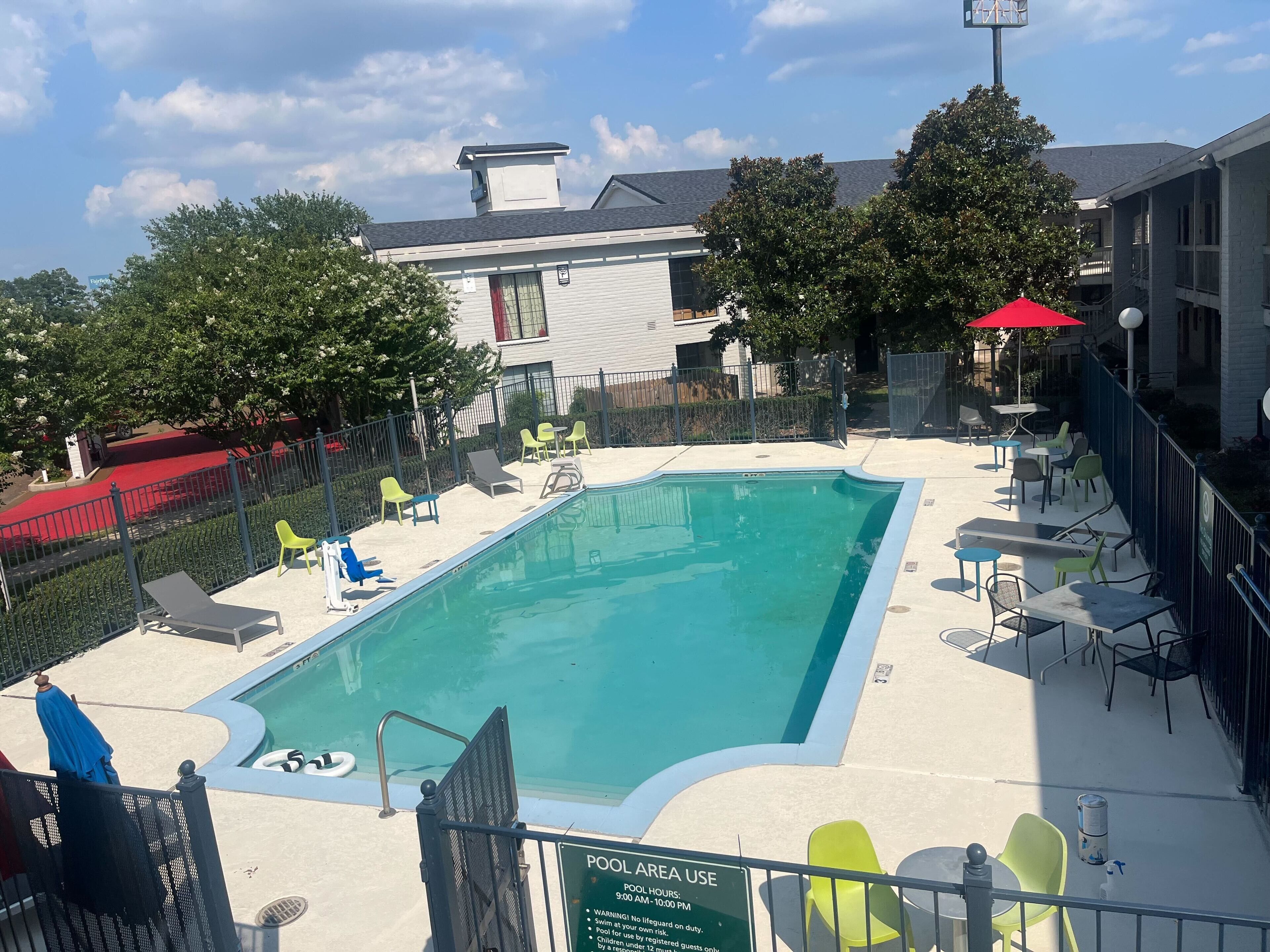 A pool area with a sign indicating pool hours and a fenced area with lounge chairs and tables.