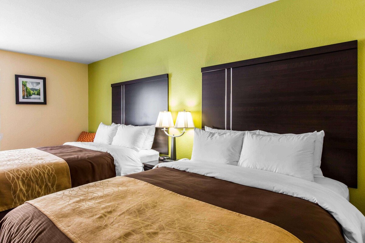 Ein Hotelzimmer mit zwei Betten, jeweils mit einer braunen Bettdecke und weißen Kissen. Dazwischen befindet sich ein Nachttisch mit einer Lampe.