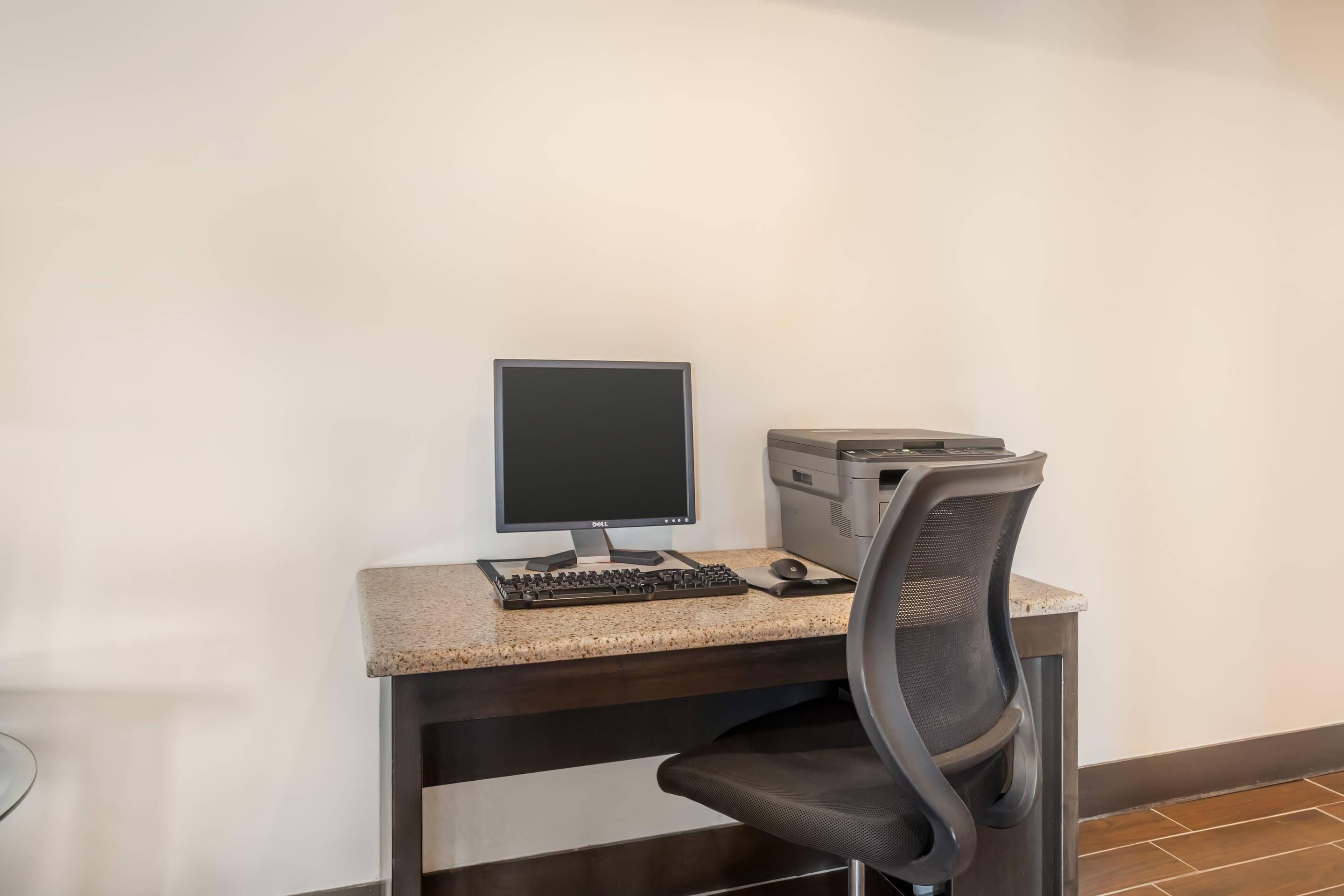 A workspace with a computer, keyboard, mouse, and printer on a granite desk.