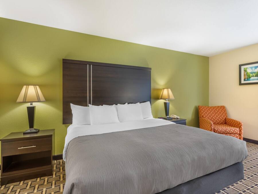 Habitación de hotel con una cama grande, dos mesitas de noche con lámparas, una silla e imagen en la pared.