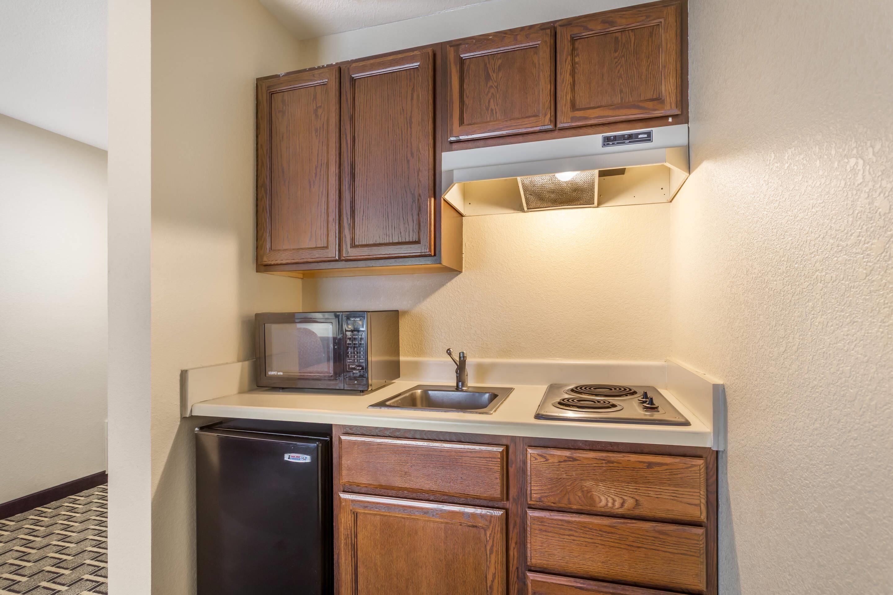A compact kitchen with wooden cabinets, a microwave, a sink, and a dishwasher.