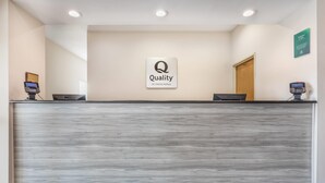 Un mostrador de recepción de hotel con un letrero de 'Quality by Choice Hotels', dos computadoras Dell y un piso de madera.