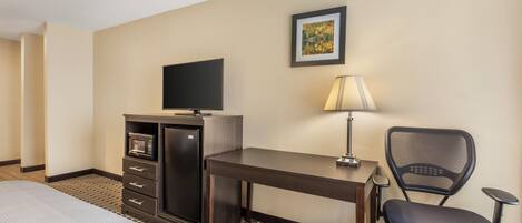 A hotel room with a bed, a desk with a chair, a television, a lamp, and a microwave.