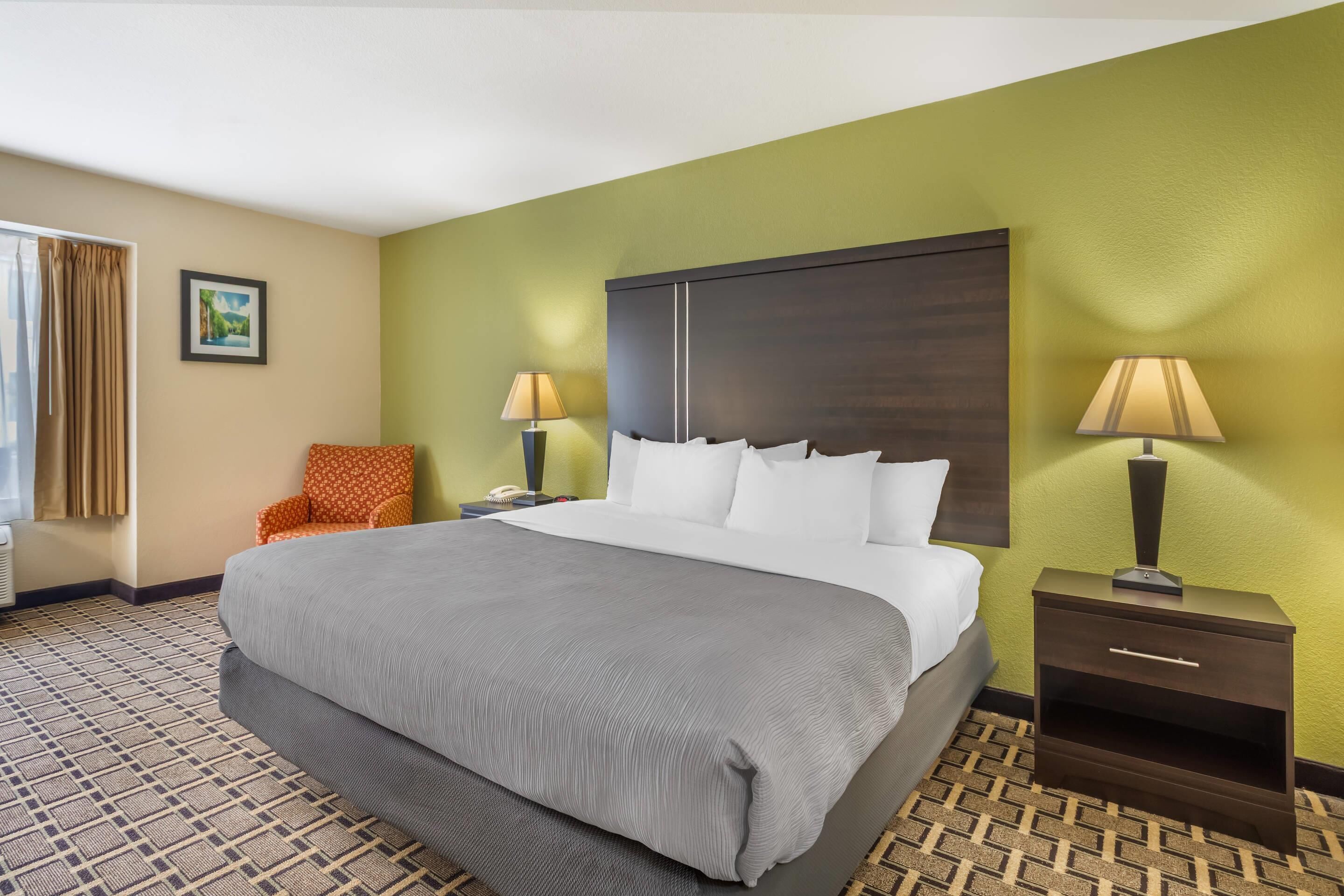 A hotel room with a large bed, two bedside tables, a chair, and a picture on the wall.