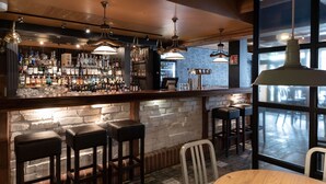Un espace bar avec un mur en briques, des tabourets en bois et des lampes suspendues.