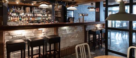 Un área de bar con pared de ladrillo, taburetes de madera y lámparas colgantes.
