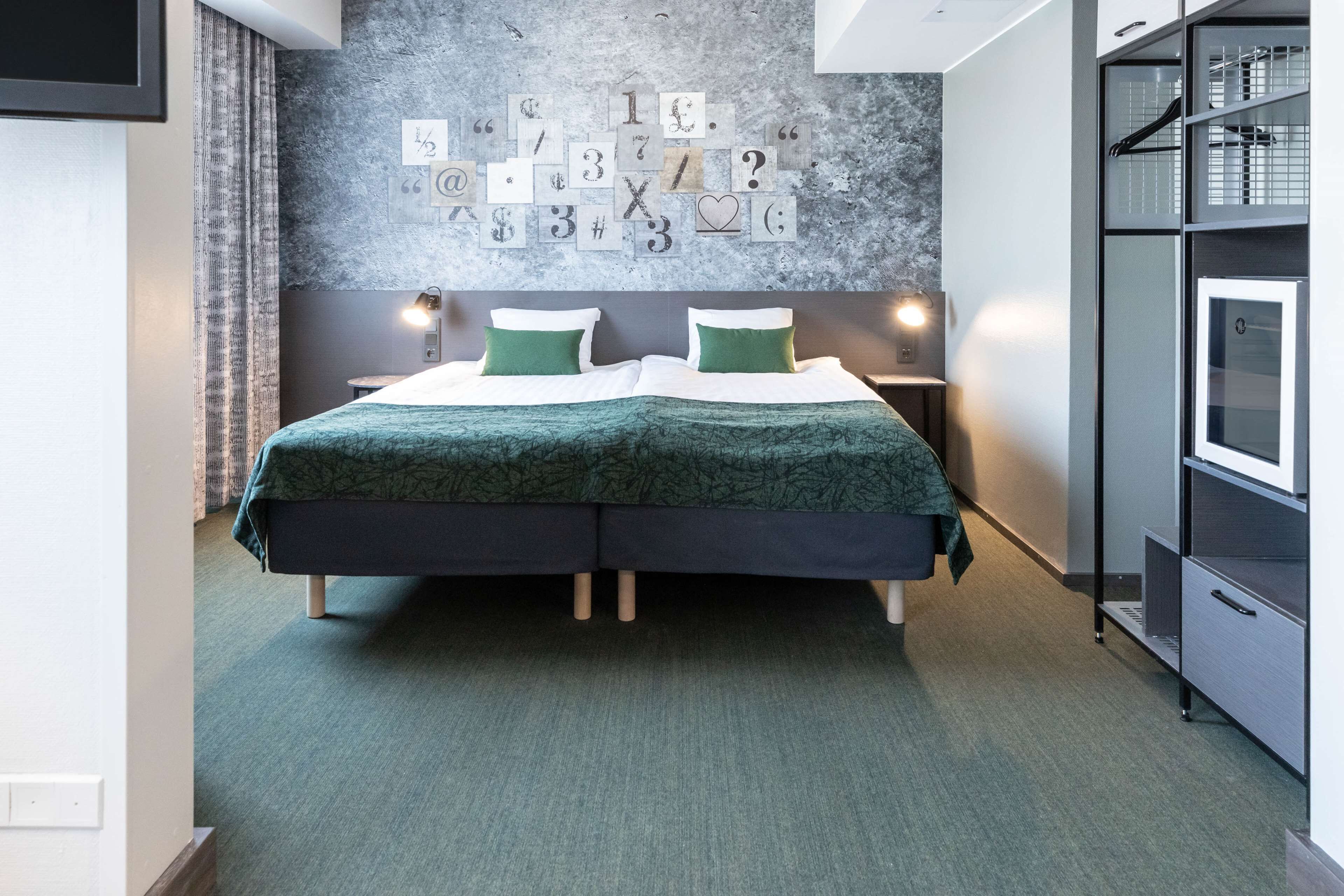 A modern bedroom with a large bed, green bedding, a wall with alphabet and number blocks, and a built-in wardrobe.