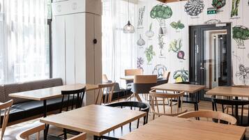 A restaurant interior with wooden tables and chairs, a black leather bench, and a wall decorated with vegetable illustrations.