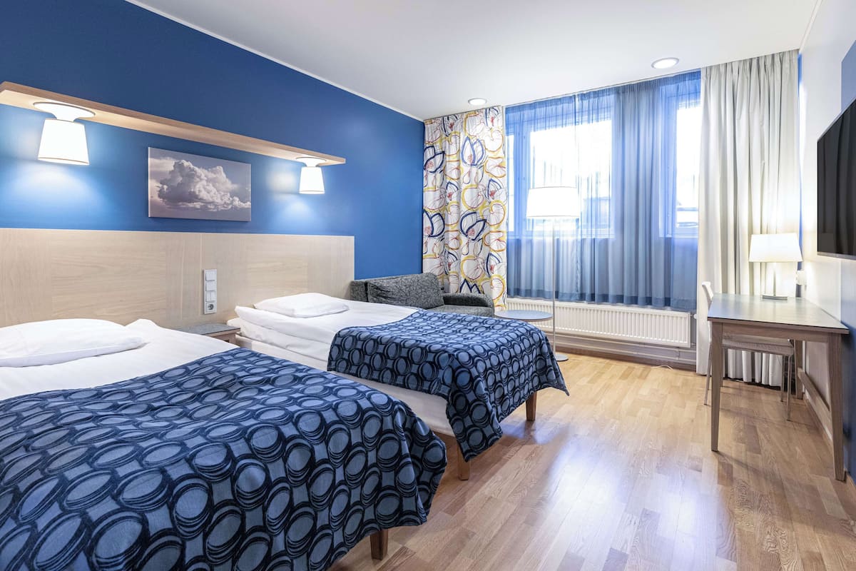 A hotel room with two beds, a desk, a chair, a TV, and a window with curtains.