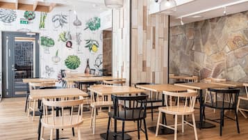 Interior de restaurante con mesas y sillas de madera, pared de piedra e ilustraciones de vegetales.