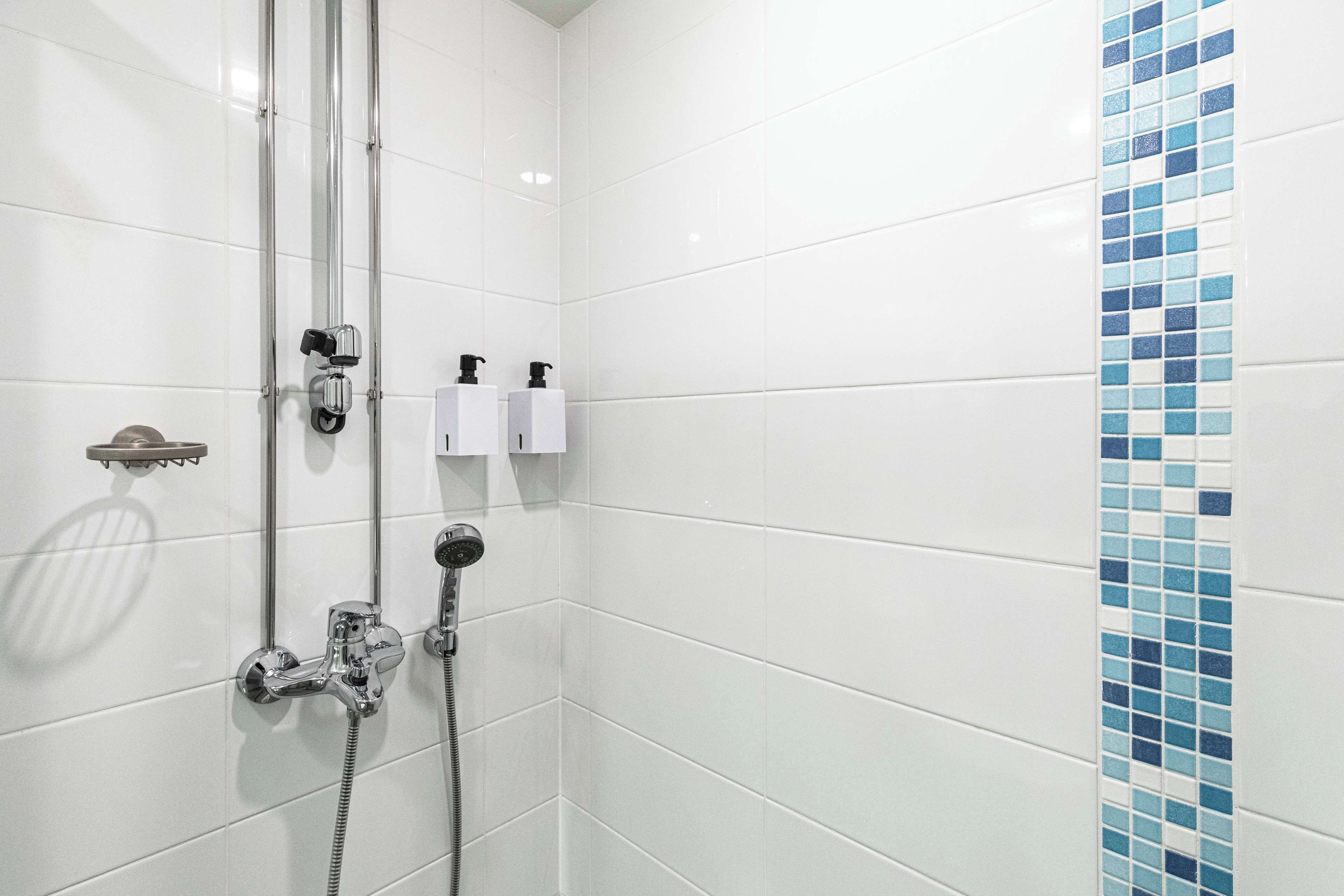 Een badkamer met witte tegels, een douche en een blauwe mozaïekrand.