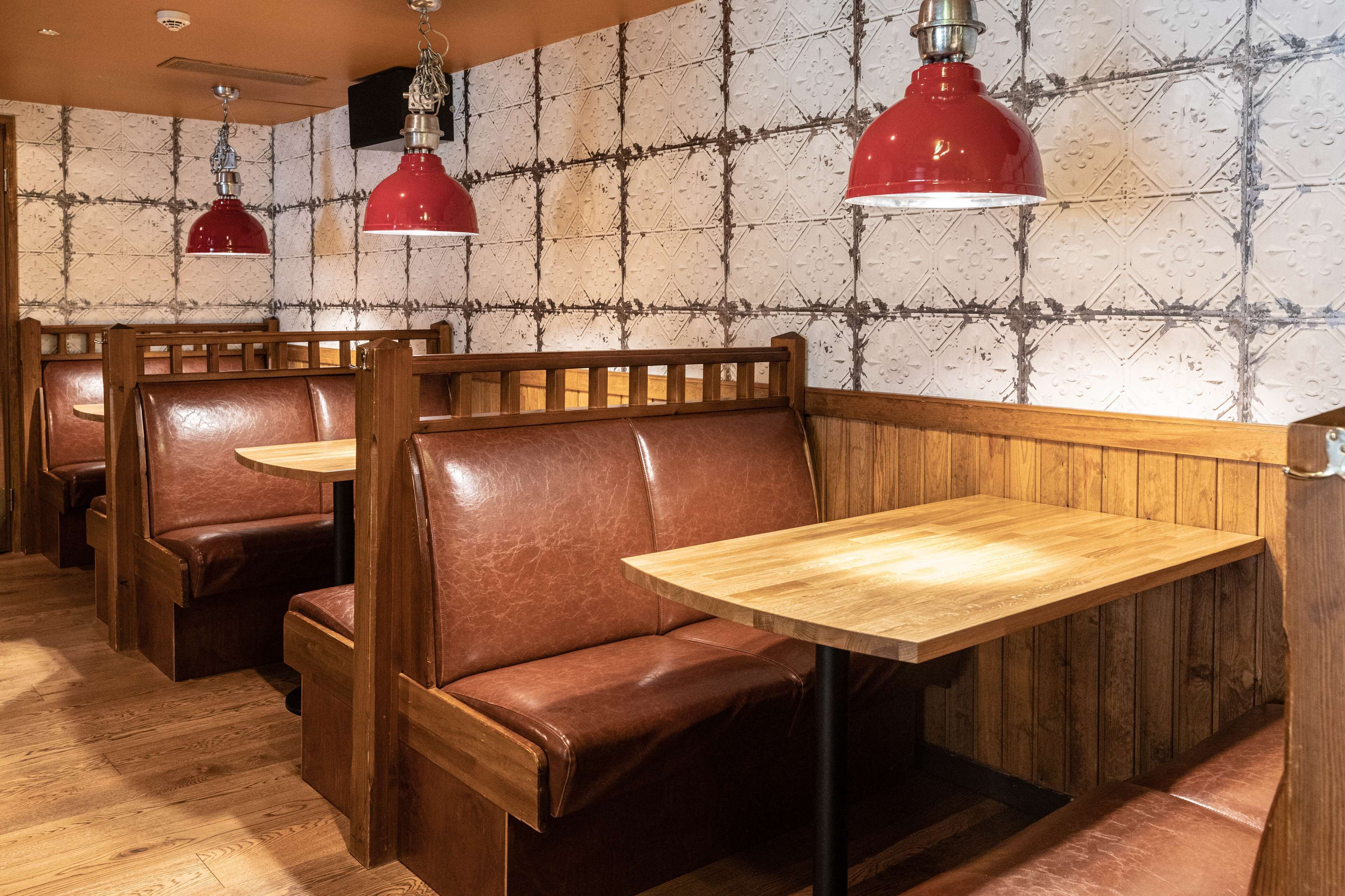 A restaurant interior with wooden booths and tables, red pendant lighting, and a patterned wall.