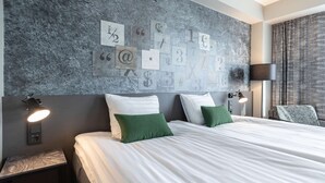 Une chambre d’hôtel avec un grand lit, deux tables de chevet avec des lampes, un mur agrémenté d’éléments décoratifs et une vue sur l’extérieur.