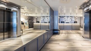 Un hall d’hôtel moderne avec un comptoir d’accueil, un espace salon et un mur décoré de motifs.