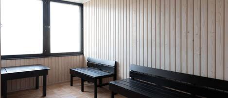 Una habitación con tres bancos negros y una mesa, paredes de paneles de madera y un ventanal grande.