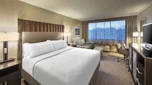 A hotel room with a large bed, a desk, a chair, a TV, and a window with curtains.