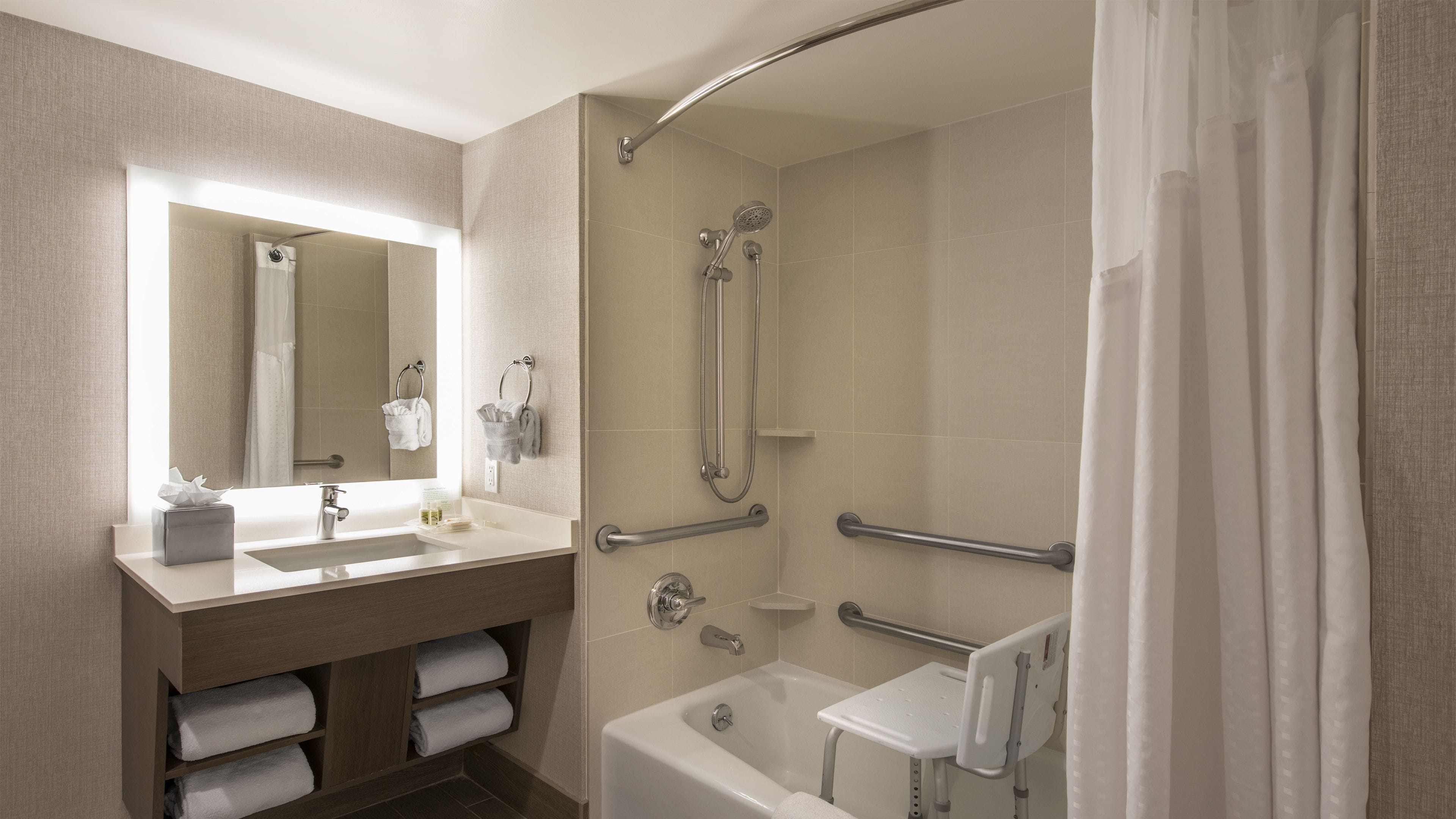 A modern bathroom with a vanity, a bathtub, a shower with a curved glass door, and a handrail.