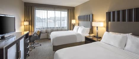 A hotel room with two beds, a desk with a TV, a chair, and a window with curtains.