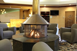 A lobby area with a central fireplace, seating arrangements, and a reception desk.