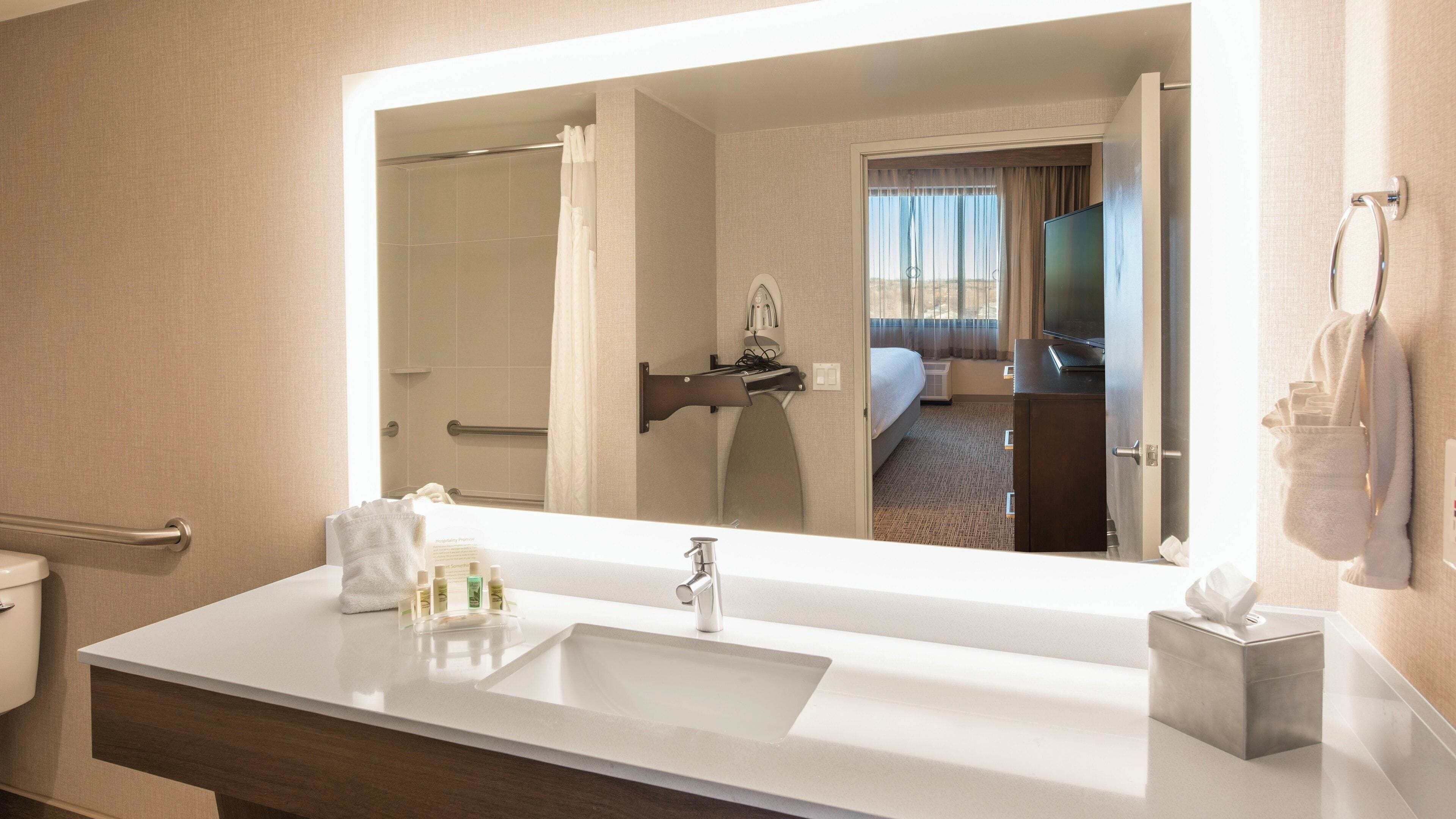 Un bany d'hotel amb un mirall gran, un lavabo, una barra de tovalloles i un vàter.